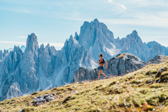 Woman trail running on a grassy mountain slope with jagged peaks