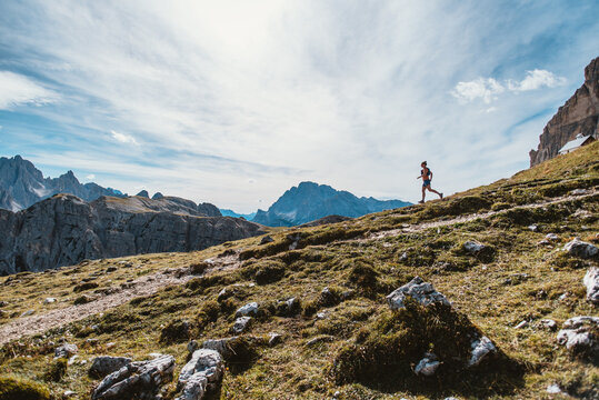 Trail runner ascends a steep grassy mountain slope with dramatic peaks