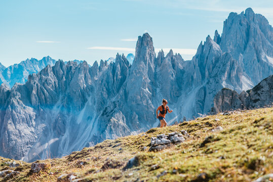 Woman trail running on a grassy mountain slope with jagged peaks