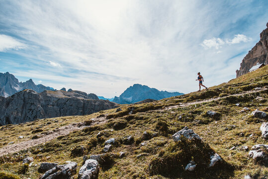 Trail runner ascends a steep grassy mountain slope with dramatic peaks