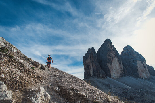 Trail runner ascends mountain path with dramatic peaks in background