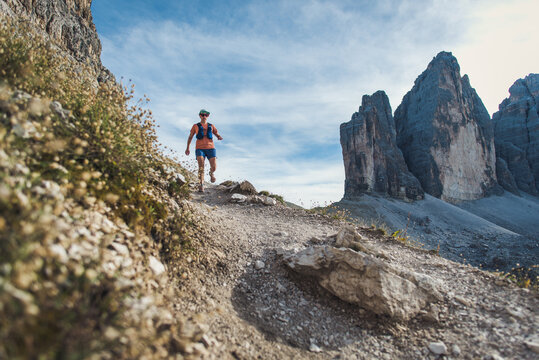 Woman trail running on a rocky mountain path with dramatic peaks