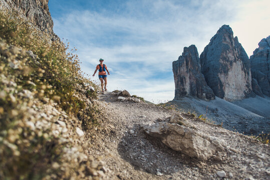 Woman trail running on a rocky mountain path with dramatic peaks