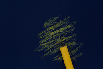 yellow oil pastel stick against abstract drawing on dark blue paper