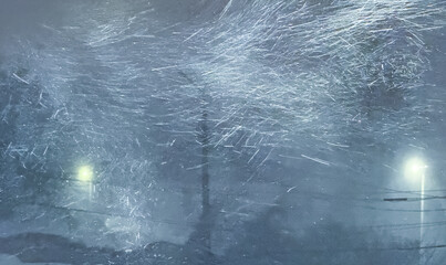 An abstract, cinematic view of a ferociously blowing blizzard at night, with swirling snow streaks caught in the bright glow of a street lamp against a dark, hazy winter background.