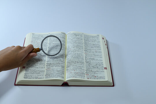 Person holding magnifying glass over English dictionary