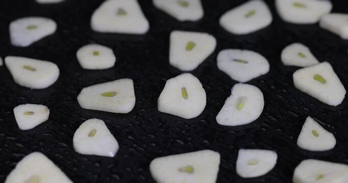 freshly peeled and sliced garlic cloves scattered on black slate, peeled and sliced fragrant natural and fresh spices from garlic cloves scattered on black slate stone, covered with drops of water