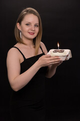 A woman in a black dress blows out a candle on a bento cake. Smoke on a black background. A girl's birthday, happiness, a gift. High quality photo