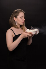 A woman in a black dress blows out a candle on a bento cake. Smoke on a black background. A girl's birthday, happiness, a gift. High quality photo