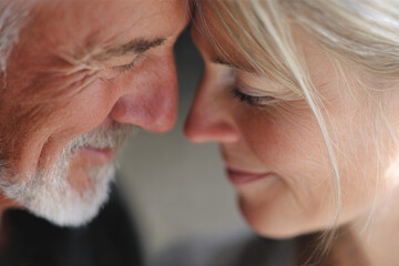Mature couple sharing an intimate moment with foreheads touching, eyes closed, serene smiles, soft lighting enhancing their emotional connection and showcasing the beauty of love and companionship