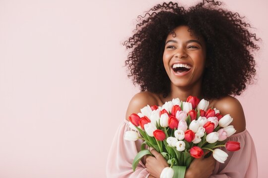 Happy young Black woman laughing while holding a bouquet of spring tulips. Joyful African American female with a flower gift on a pink background with copy space