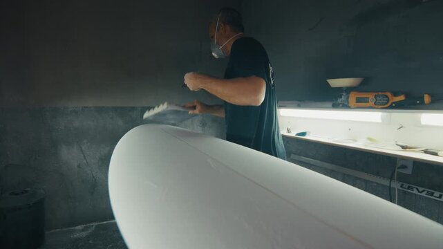 Surf factory. Adult male shaper creates the surfing board on the factory