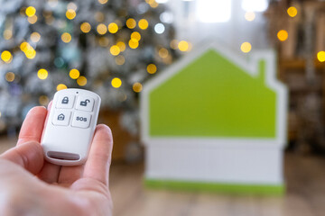 Security System Keychain in hand on background fairy lights Christmas tree and tiny house gift for New Year, Christmas. Home security, alarm system, SOS signal, protection from thieves