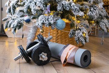 Sports equipment dumbbells, a fitness mat, and fitness bands lie under the Christmas tree at home as a gift for Christmas and New Year