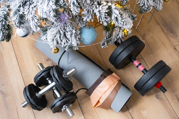 Sports equipment dumbbells, a fitness mat, and fitness bands lie under the Christmas tree at home as a gift for Christmas and New Year