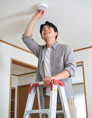One happy Korean man checking smoke detector at ceiling, safety concept.