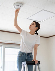 One happy Korean woman checking smoke detector at ceiling, safety concept.