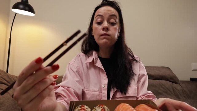 Woman enjoying a takeout sushi meal at home with chopsticks, looking satisfied