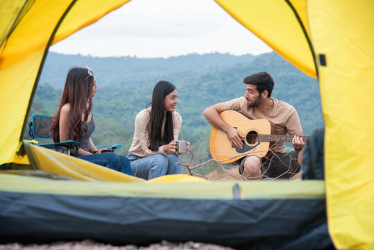 Group of three people sitting outside the yellow tent having fun conversation, friends are engaged sitting relaxation free time after hiking outdoors activities fall season, tourist friends traveling