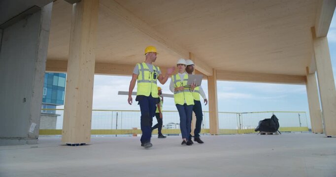 Three Professional Construction Engineers Walk Through an Upper Floor of Commercial Residential Building, Discussing Structural Details on a Laptop, Real Estate Development Business Property Project.