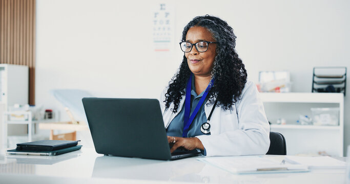 Doctor, black woman or reading with laptop in hospital office, digital resources or healthcare database. Medical archive, research or mature physician with pc for telehealth, patient admin or info