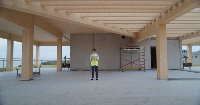 Female Engineer Wearing VR Headset Inspects Open‑plan Commercial Residential Construction Site, Virtually Reviewing Real Estate Development Details, Gesturing and Walking Through Building Interior