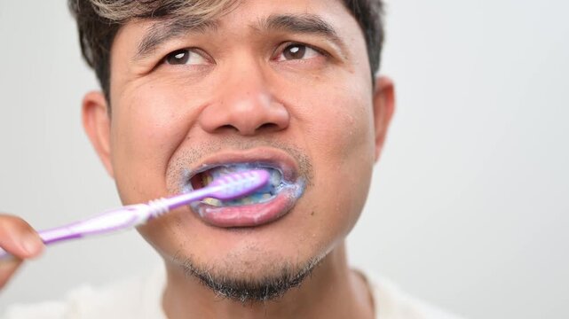 Close up video of an Asian adult man brushing his teeth with toothpaste foam. Clear view of teeth and mouth during daily oral hygiene routine, dental care and personal healthcare concept.