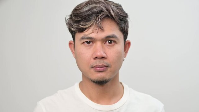Video portrait of an Asian adult man with neutral face slowly nodding head. Agreement, understanding, approval and confirmation concept in everyday lifestyle.