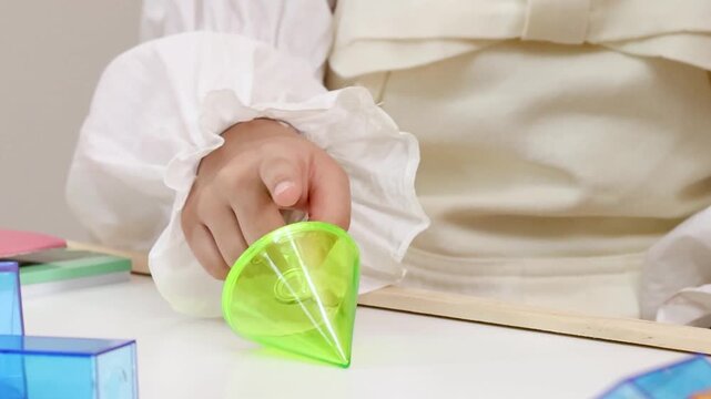 Close Up of Child Spinning Translucent Green Cone on White Table