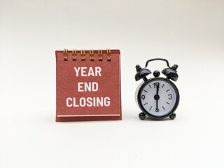 YEAR-END CLOSING word alphabet letters on a calendar next to black alarm clock, isolated on white background 