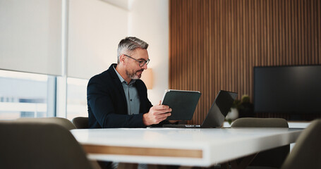 Obraz premium Business, man and reading with tech in office for research, financial report and budget comparison. Mature person, tablet and laptop for accounting, finance results and information for investment