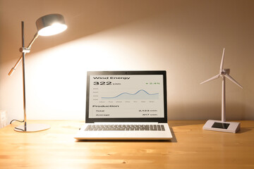 Laptop showing wind energy production data and efficiency trends, paired with a small wind turbine model, symbolizing renewable resource management and smart home energy consumption