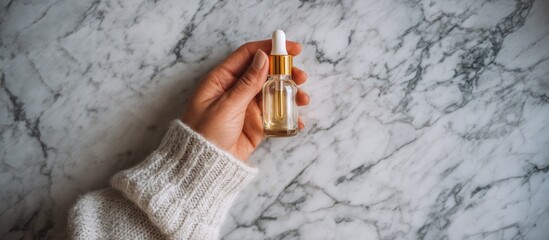 Hand holding a dropper bottle of serum on a marble background.