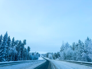 Winding asphalt road through a snowy winter landscape, wet highway with frozen trees and cloudy sky in a cold northern forest