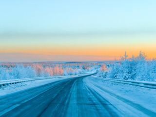 Empty Asphalt Highway Stretching Through a Frozen Winter Forest with Golden Sunset Light on Tree Tops