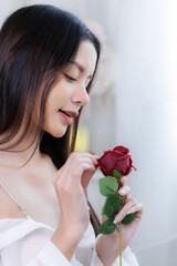 Close up side profile of Asian woman smiling while touching red rose petal with finger