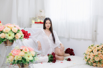 Beautiful Asian woman sitting on floor surrounded by pastel and red rose bouquets