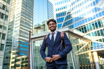 Fototapeta premium Young businessman smiling, carrying backpack in modern city