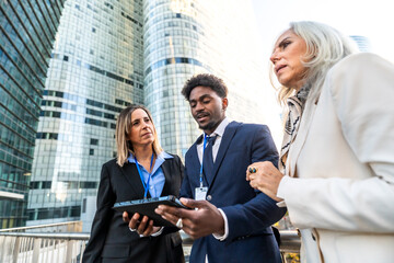 Diverse business professionals discussing work using digital tablet outdoors