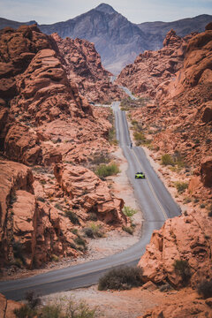 View of a sinuous asphalt ribbon winding through fiery sandstone formations towards a distant, stoic peak in Valley of Fire State Park, Overton, Nevada, United States.