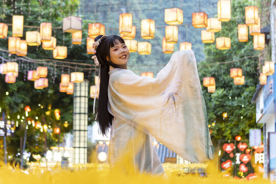 View of a smiling girl in traditional clothing twirling beneath a canopy of glowing lanterns in a vibrant, golden light, Guilin, Guangxi, China.