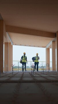 Vertical Screen: Two Male Construction Workers Walk across Commercial Construction Site, Talk about Engineering Details for Residential and Business Real Estate Development and Construction Planning.