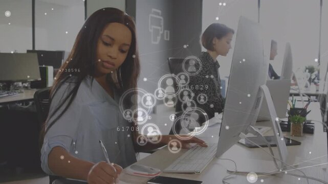 Animation of profile icons over african american woman taking notes and using computer at office