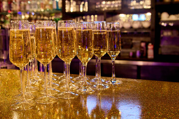 Champagne flutes filled with sparkling wine on a glittering surface in warm festive lighting, creating an elegant celebration atmosphere suitable for parties, events, and New Year concepts.