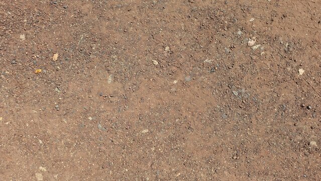Dirt road. Brown small stone floor texture background. Rural roads or pavements are used for travel. Close-up aerial view of rough brown soil with no vegetation.