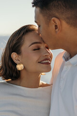 A close-up of a happy young couple. A man kisses a woman on the forehead. The concept of love and tenderness.