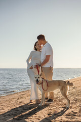Happy young couple with a dog on the beach. Pregnant woman with a man and a dog on a walk, family