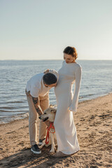 Happy young couple with a dog on the beach. Pregnant woman with a man and a dog on a walk, family
