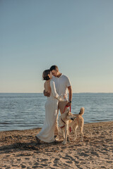 Happy young couple with a dog on the beach. Pregnant woman with a man and a dog on a walk, family