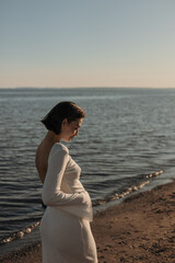 A young pregnant woman is walking on the beach in the evening. The concept of motherhood and childbirth
